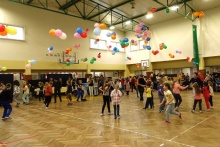 Sala gimnastyczna udekorowana balonami pełna tańczących dzieci i seniorów